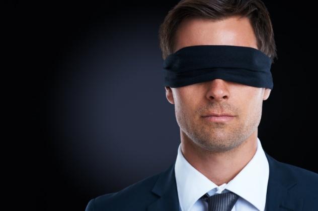 Shot of a blindfolded young businessman standing against a black background