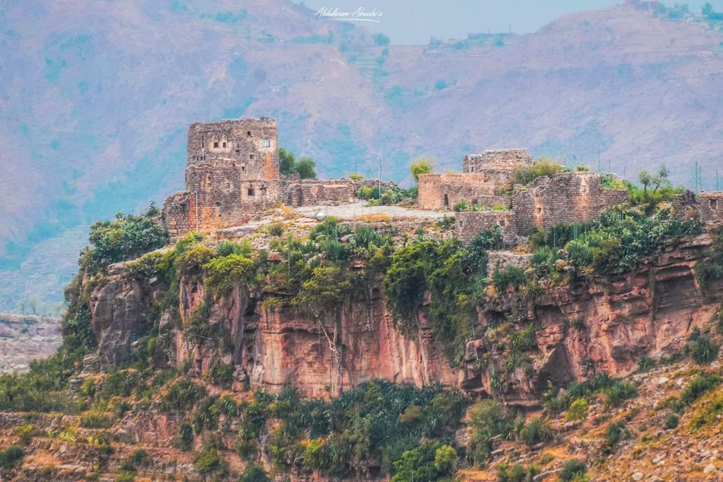يظهر لنا في الصورة جبل الرنع الذي يقع في مدينة حجة، وتظهر لنا بيوت مبنية فوق هذا الجبل الأخضر 
