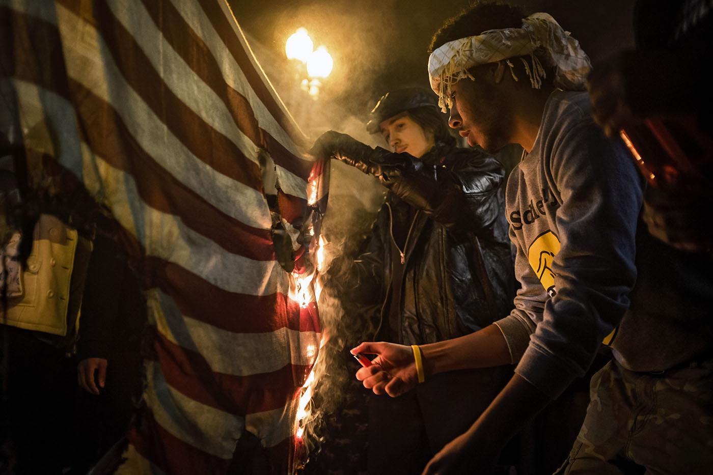 Protesters burn a US flag as they march through downtown Washington, DC following a Missouri grand jury's decision not to indict Officer Darren Wilson in Washington