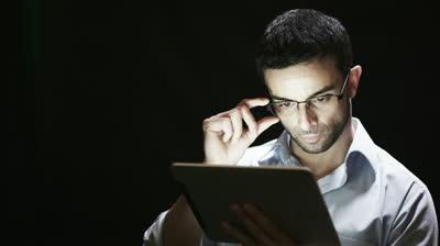 stock-footage-close-up-of-young-man-reading-his-tablet-in-the-dark-black-background